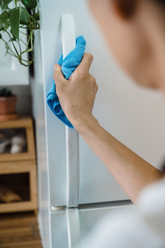Close-up of a hand cleaning a refrigerator door handle with a blue cloth