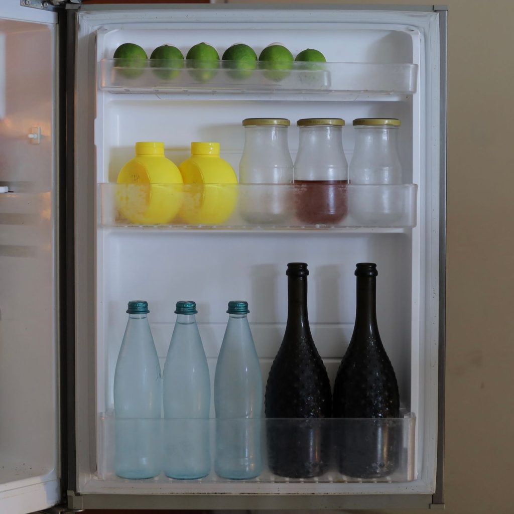 Open refrigerator with bottles, limes and neatly organised shelves