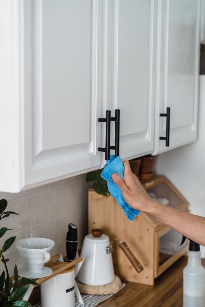 Person wiping white kitchen cabinets with a blue cloth