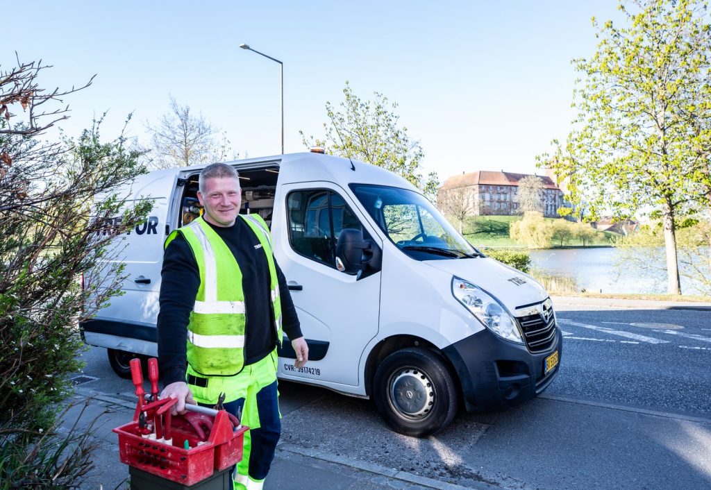Smiling service technician standing beside a work van holding his tools