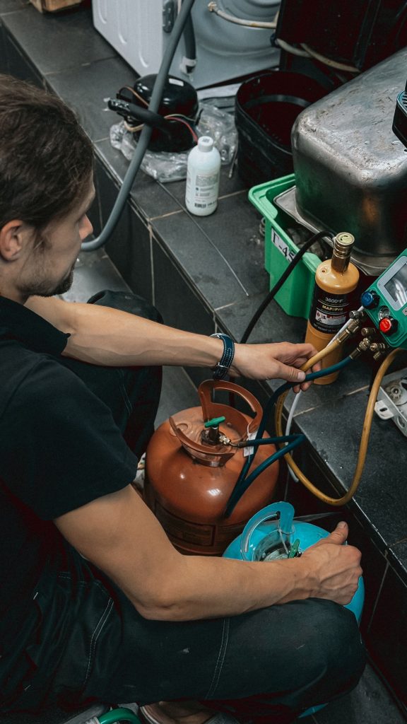 Technician handling refrigerant cylinders and gauges in a workshop