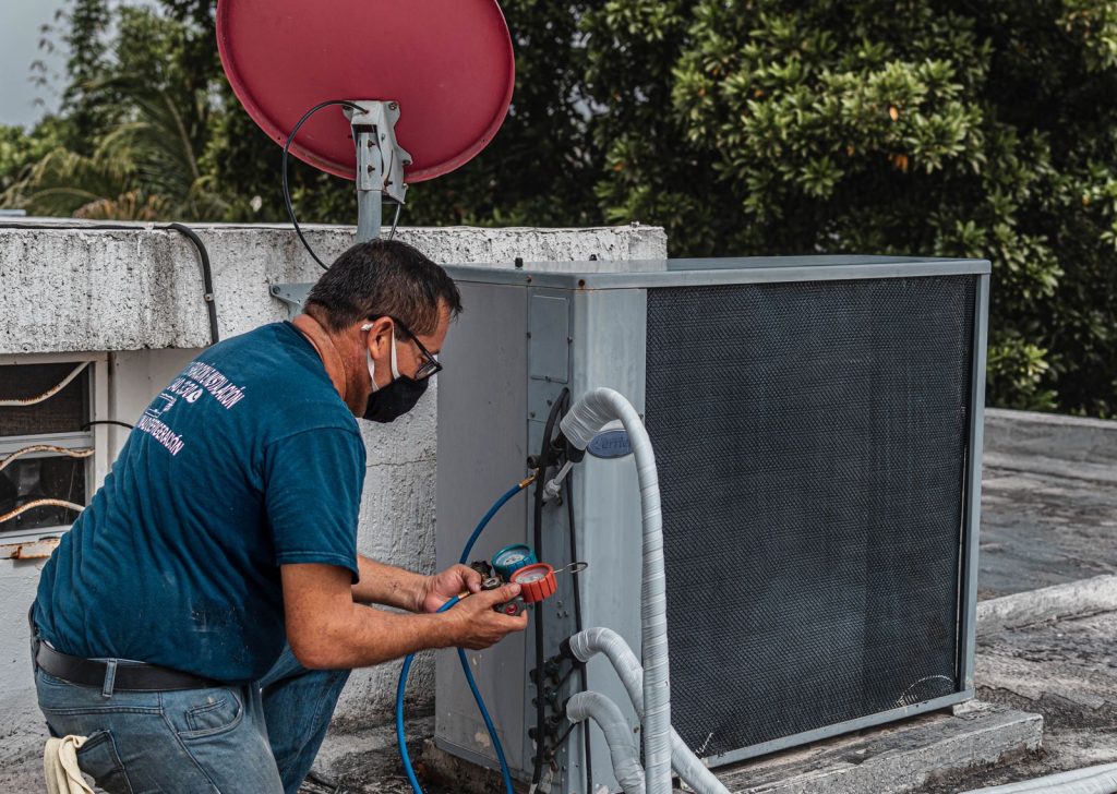 Technician in a face mask repairing a cooling unit with a manifold gauge