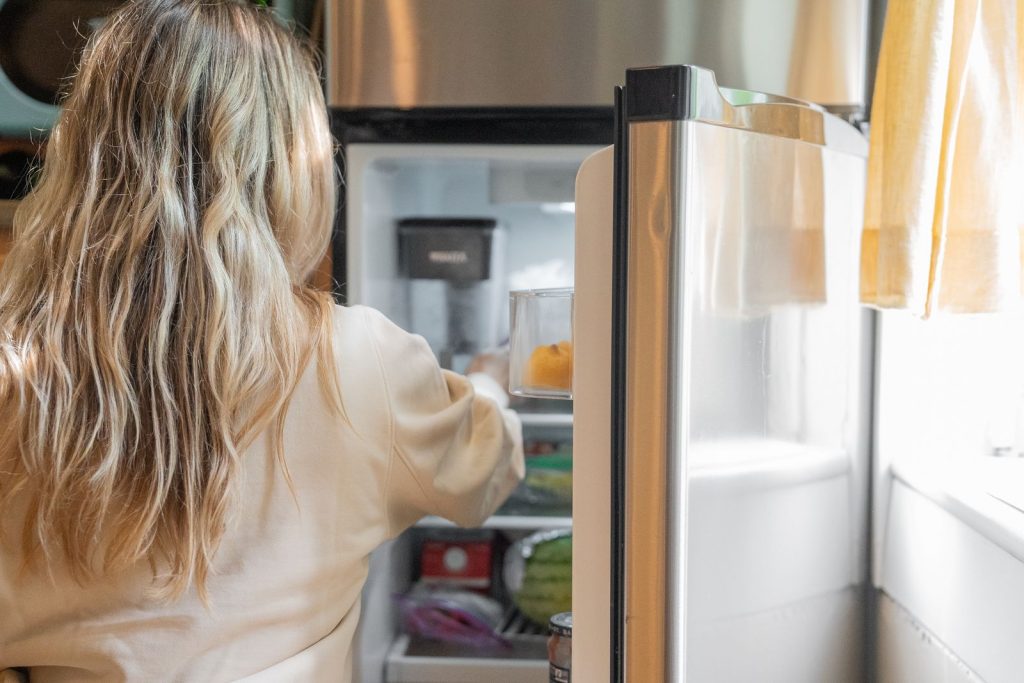 Woman taking fresh food from a working refrigerator in a bright kitchen